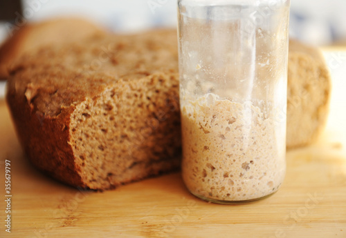 Freshly baked homemade rye-wheat whole grain bread and rye sourdough in a glass jar. Close up