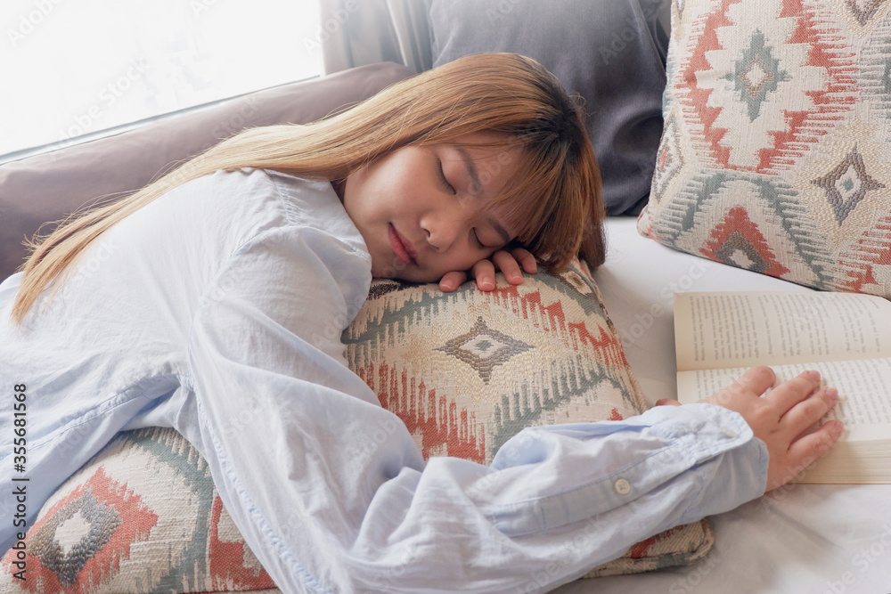 An asian woman napping comfortably in bed with a book in hands. Resting at home.