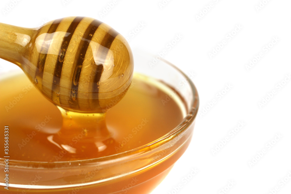 Honey flowing from a wooden stick into a bowl isolated on a white background