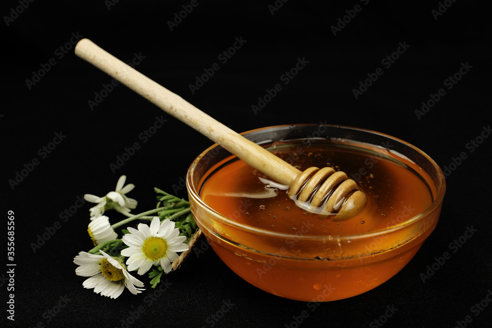Honey in a bowl with a wooden stick, wildflowers on a black background Honey in a bowl with a wooden stick, wildflowers on a black background