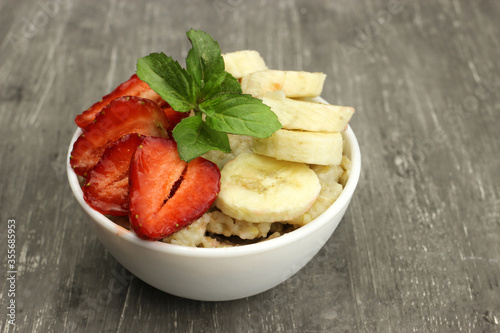 Bowl of oatmeal with a banana, strawberries and mint on a gray background. Fresh healthy Breakfast