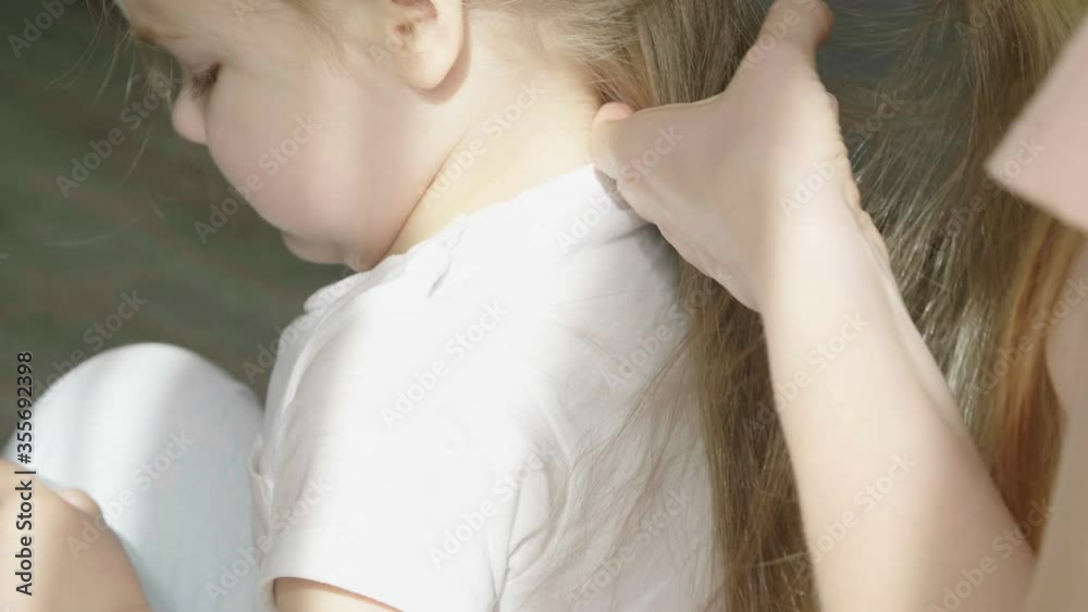 Caring mum braiding little daughter's hair, love and care. Mom braids the braid of her little daughter. Caring mum braiding little daughter's hair, love and care. Mom braids the braid of her little daughter.