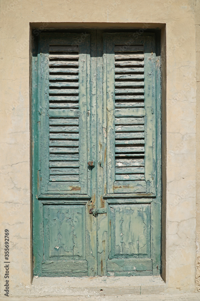 Green shuttered doors with peeling paint with bright sunshine casting deep shadows Green shuttered doors with peeling paint with bright sunshine casting deep shadows