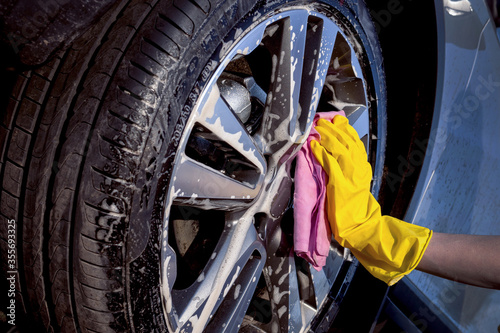 A man washes a car. Wheel in soapy foam.