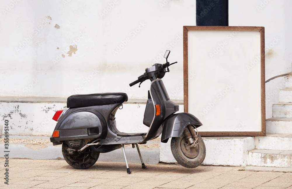 An old gray-black retro scooter is parked on a Zanzibar street near a frame or table. A place to write text.
