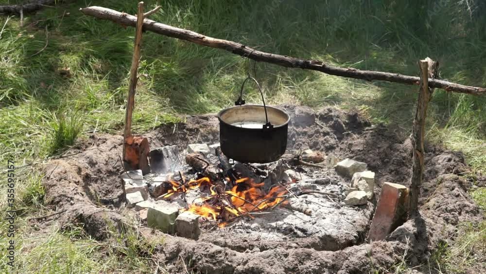 Tourist bowler on the crossbar at the stake. Tongues of flame warm the smoked bottom of the pot. Tourist bowler on the crossbar at the stake. Tongues of flame warm the smoked bottom of the pot.