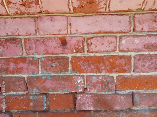 Brick wall. Red brick painted with front beige paint. Paint is missing in some places. Looks through the structure of the brick and cement mortar.