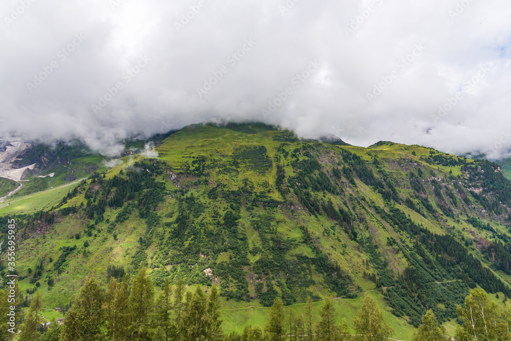Tall green mountain covered with forest under huge white cloud