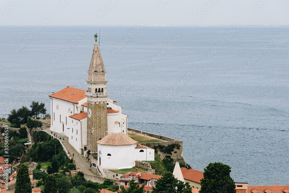 Saint George Cathedral in Piran with calm sea on the background and green trees nearby