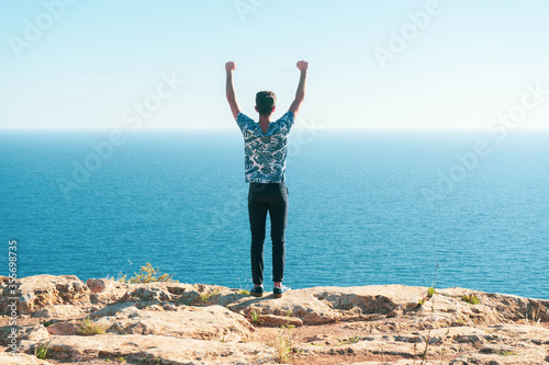 Young man with open arms looking at the sea on the horizon.
