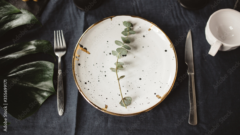 plate with cutlery on a black table and green leaves plate with cutlery on a black table and green leaves