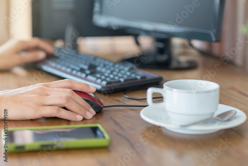 Woman's hand clicking on mouse with a cup of coffee besides on wooden table.Female office worker clicking on mouse