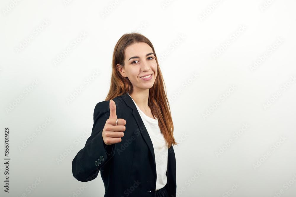 Showing thumb up, like sign positive something good has happened finger gesture for fine result well done. Young attractive woman with brown hair in a light t-shirt, black jacket on white background Showing thumb up, like sign positive something good has happened finger gesture for fine result well done. Young attractive woman with brown hair in a light t-shirt, black jacket on white background