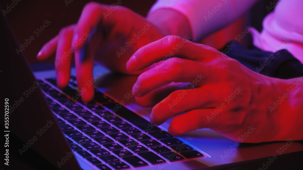 Macro shooting, men's fingers, which print on a laptop, evening muted bluered light