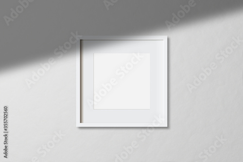 Minimal empty square white frame picture mock up hanging on white wall background with window light and shadow. isolate image