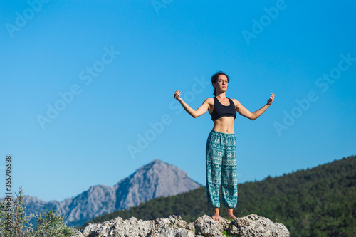 Girl practices yoga on top of the mountain.