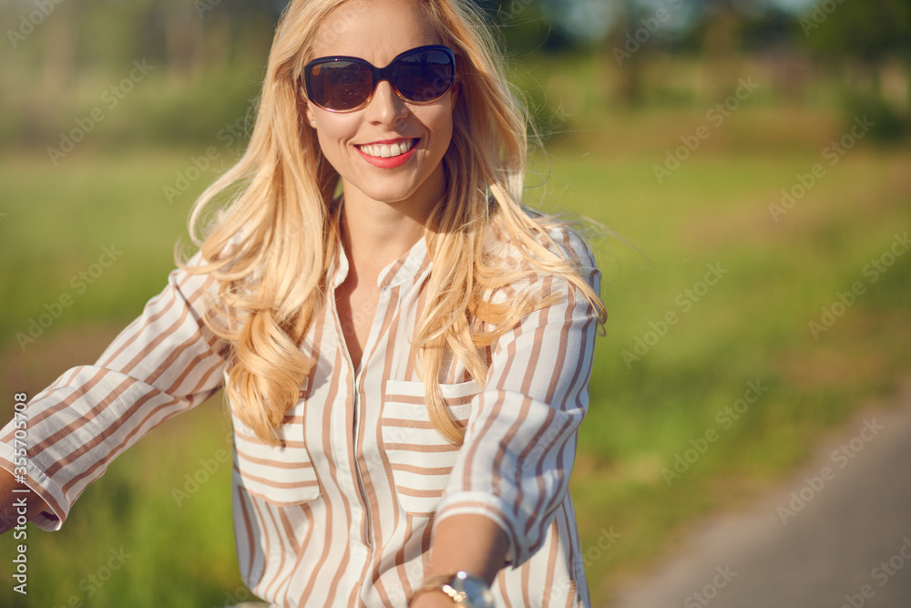 Portrait of a beautiful woman smiling happy while wearing a striped shirt and riding a bicycle in the countryside in a sunny day Portrait of a beautiful woman smiling happy while wearing a striped shirt and riding a bicycle in the countryside in a sunny day