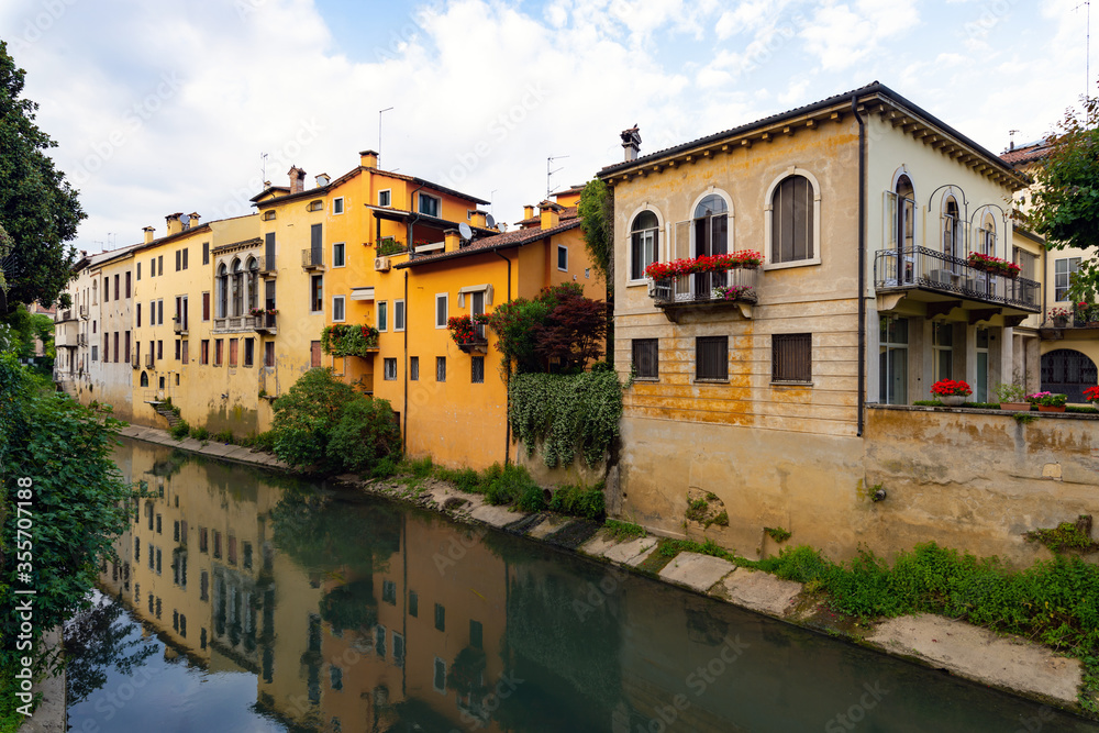 Buildings of various eras and architectural styles along the banks of the Retrone river in the city of Vicenza. Some are restored others worn out. Reflections on the water, spring afternoon. Italy.