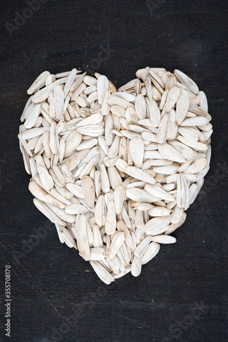 Fotografía Organic yellow sunflower seeds in heart shape on black background