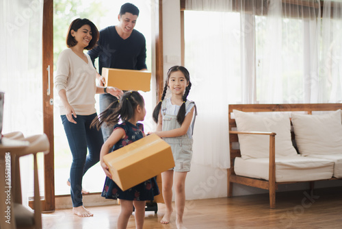 Young Asian family with daughter holds carton and walking in to a new home in moving relocation day which Excited smiling and felling happy. Mother Father and daughter move on a new home concept.