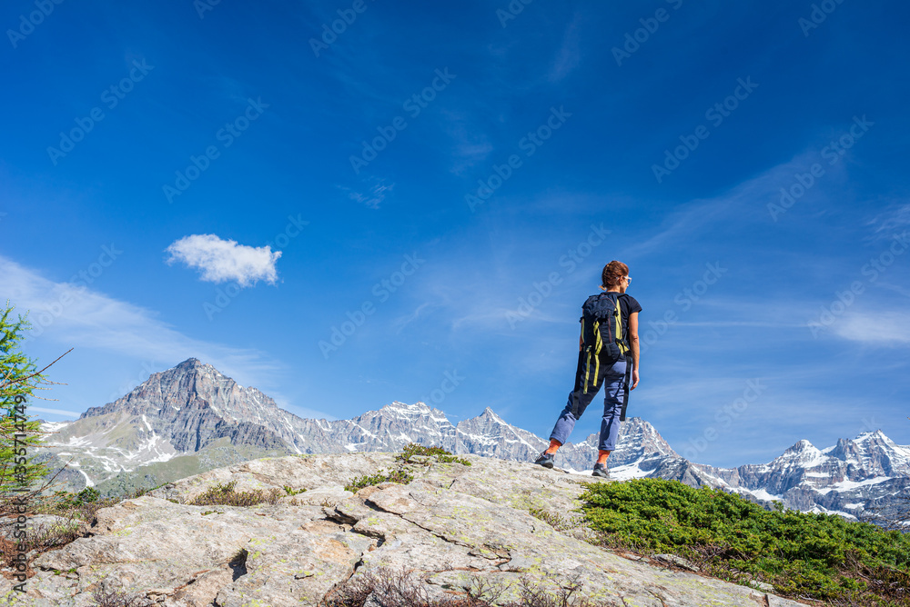 Woman with backpack on mountain top. One person looking at scenic alpine landscape summer vacation fitness wellbeing freedom concept