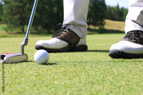 Golf player at the putting green hitting ball into a hole.