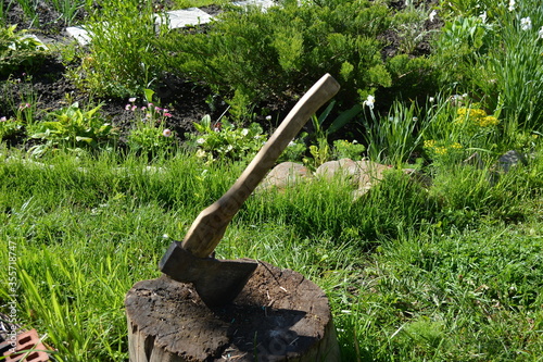 Close up of an old axe with a wooden handle stuck in a stump in the yard of a country house