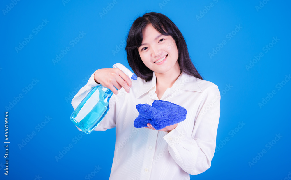 Asian Woman cleaning and polishing the kitchen worktop with a spray detergent, housekeeping and hygiene concept, accessories studio shot isolated on blue background 
