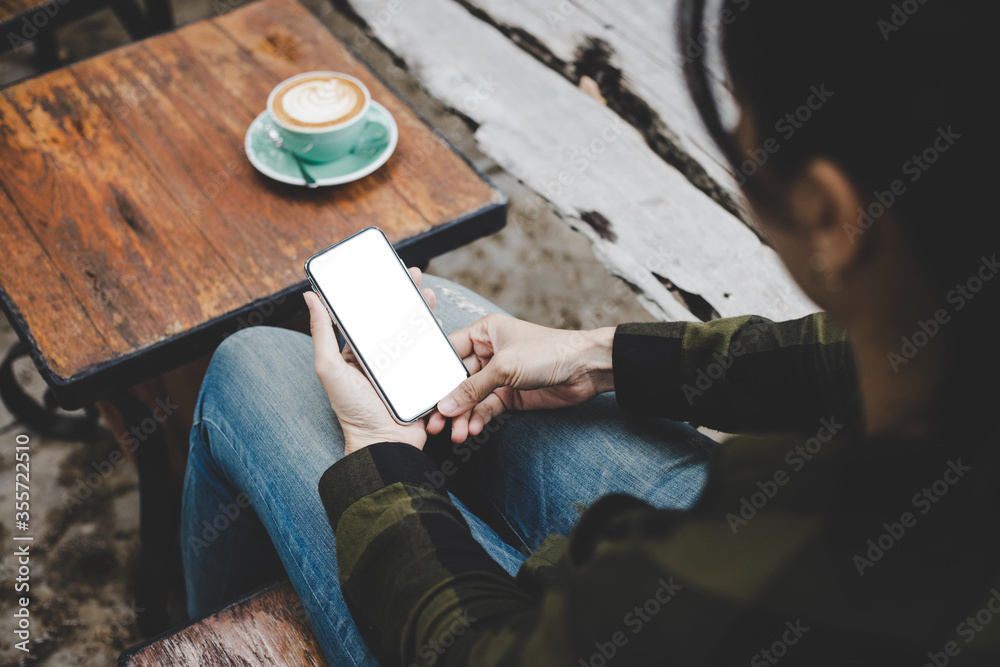 Fototapeta premium cell phone mockup image blank white screen.woman hand holding texting using mobile on desk at coffee shop.background empty space for advertise.work people contact marketing business,technology
