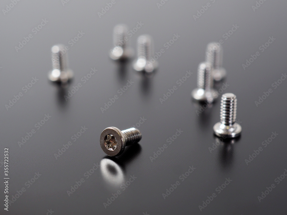 Fototapeta premium A group of white bolts on a dark matte surface. One of them lies, the others stand. Illustration of small light screws close-up. Assembly and repair of electronic equipment and computer hardware