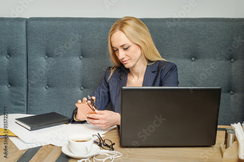 Young business woman is using smartphone sitting at table in cafe.