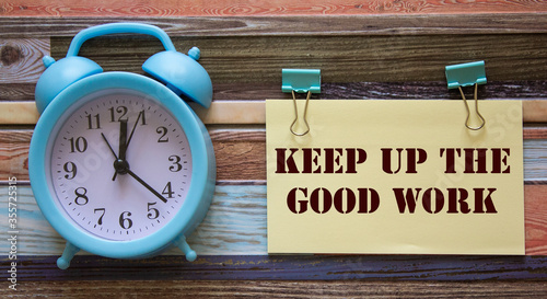 On a wooden background, an alarm clock and text keep up the good work. photo