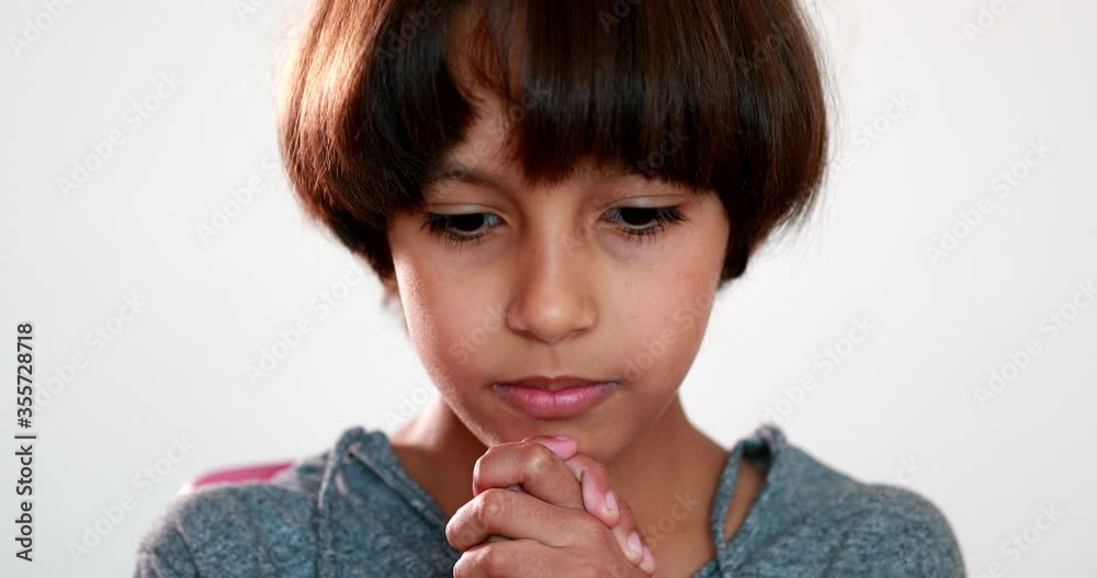 Child boy praying to God with hands held together with closed eyes