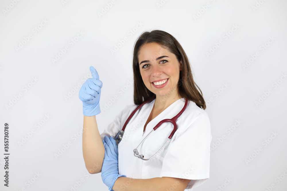 Young beautiful woman standing over white isolated background wearing her doctor uniform and doing the ok signal with her finger Young beautiful woman standing over white isolated background wearing her doctor uniform and doing the ok signal with her finger