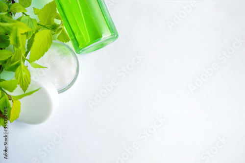 Face cream in a glass jar, slices of fresh cucumbers, green refreshing gel in a bottle on a white background. Fresh leaves. Spa treatments. View from above. Copy space