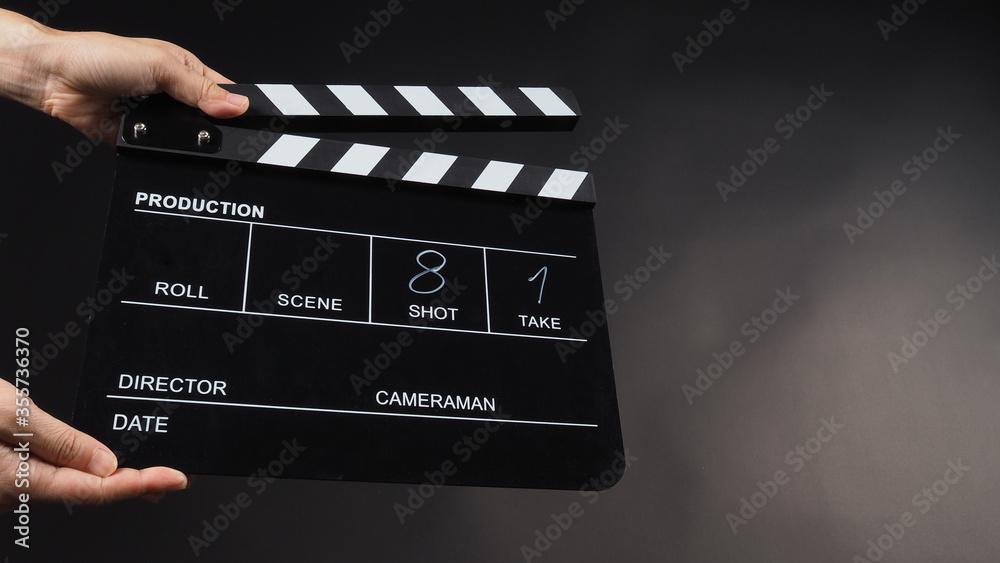 A Hand is holding Black clapper board or movie slate use in video production, movie, film, cinema industry on black background. It has written in number.