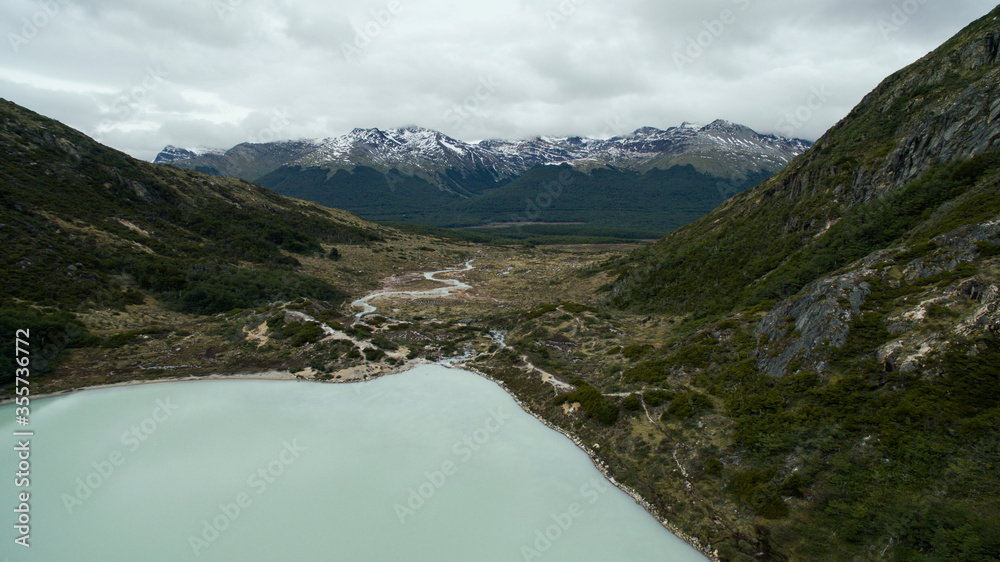 Aerial view of Laguna Esmeralda in Ushuaia, Tierra del Fuego, Patagonia Argentina. Turquoise glacier water lake and stream flowing downhill across the valley and forest into the Andes mountains