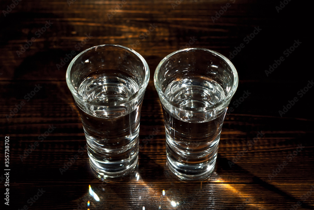 Glasses with alcohol close up. Vodka on a brown wooden background. Glass table from worn shabby boards.