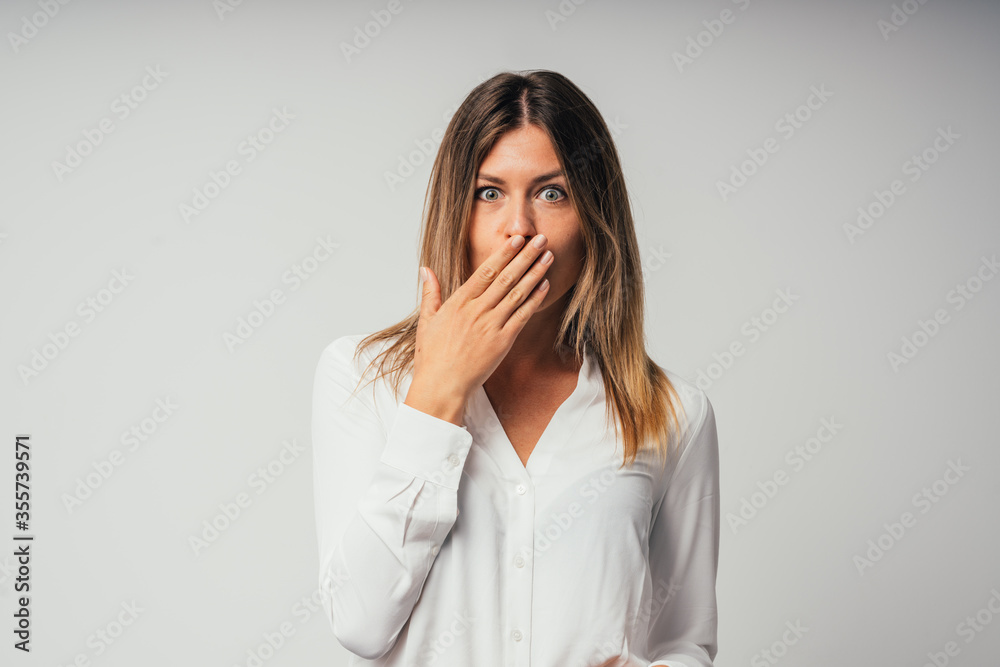 portrait of young beautiful surprised and amazed girl with hand in front of mouth isolated on gray background portrait of young beautiful surprised and amazed girl with hand in front of mouth isolated on gray background