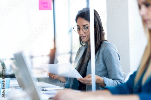 Two business women work with laptops on the partitioned desk in the coworking space. Concept of social distancing. photo