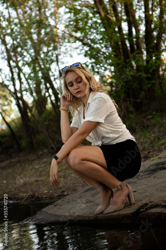 Girl near the water. A blonde woman in a white shirt poses on the Bank of a river or lake.