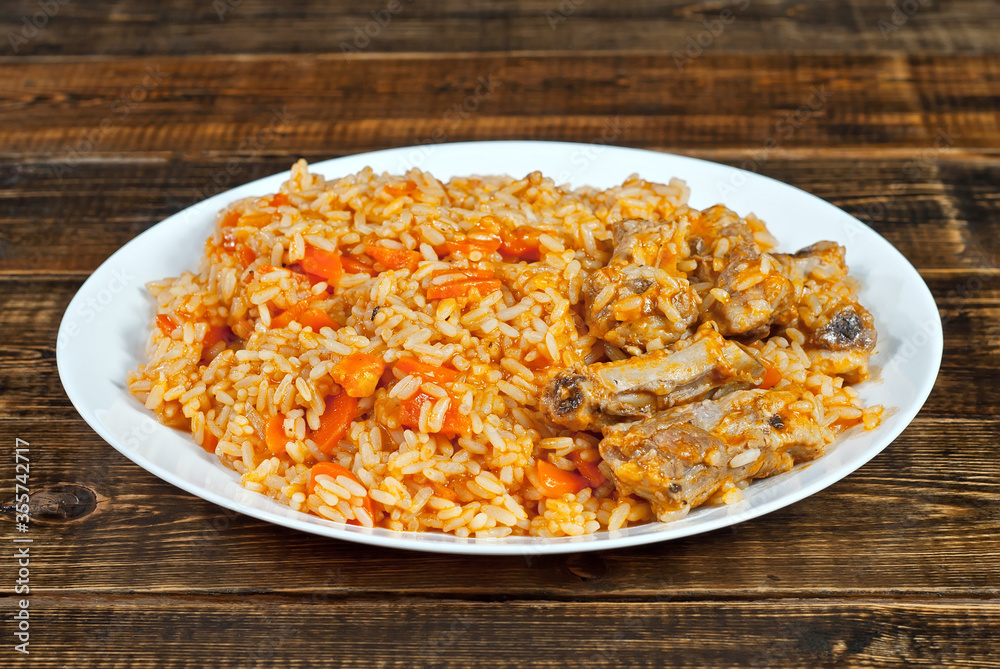 Pilaf with meat and carrots in a green plate. Rice on a brown shabby board. Pilaf with meat and carrots in a green plate. Rice on a brown shabby board.