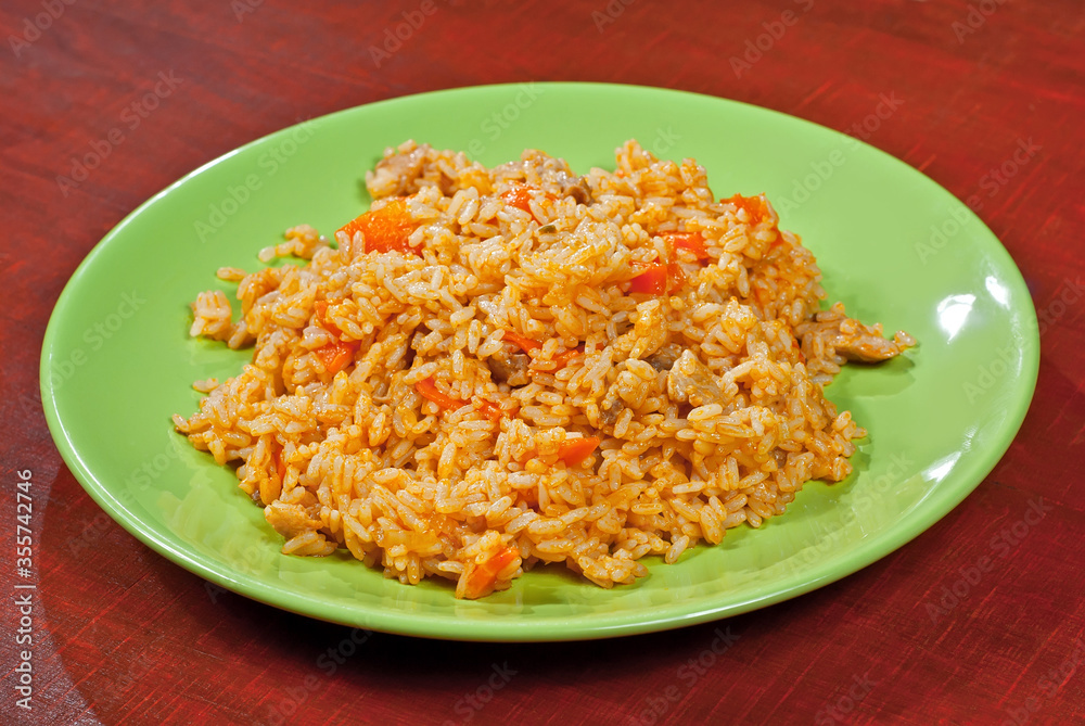 Pilaf with meat and carrots in a green plate. Rice on red plywood.