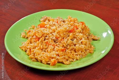 Pilaf with meat and carrots in a green plate. Rice on red plywood.