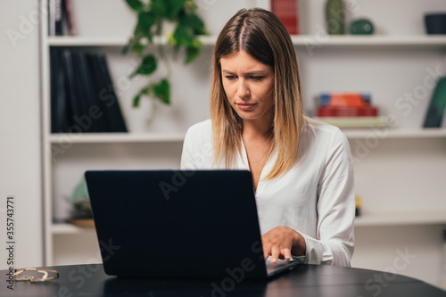 Head shot caucasian girl sitting at table. Stressed woman in office working on the computer. Headache concept. message email with bad news.