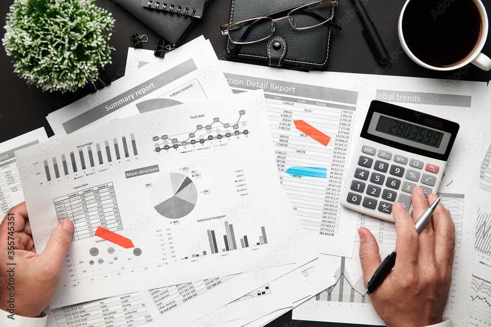 Top view of businessman's hands working with financial reports. Modern black office desk with notebook, pencil and a lot of things. Flat lay table layout. Top view of businessman's hands working with financial reports. Modern black office desk with notebook, pencil and a lot of things. Flat lay table layout.