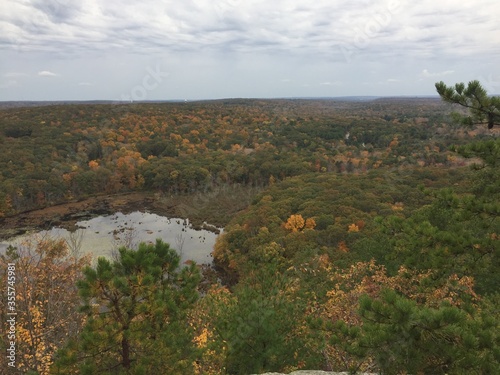 View over the edge of a cliff on a mountain on Lantern Hill trail in Connecticut, with a pond below in the distance 