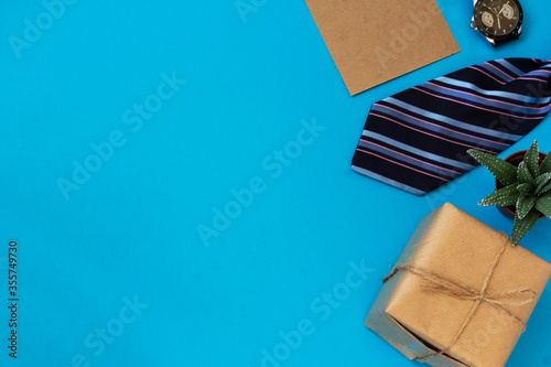 Happy fathers day gift layout on a blue background. Greeting card with a side border of gifts, ties and a wristwatch, a green flower of a succulent in a pot in a layout. Top view with copy space