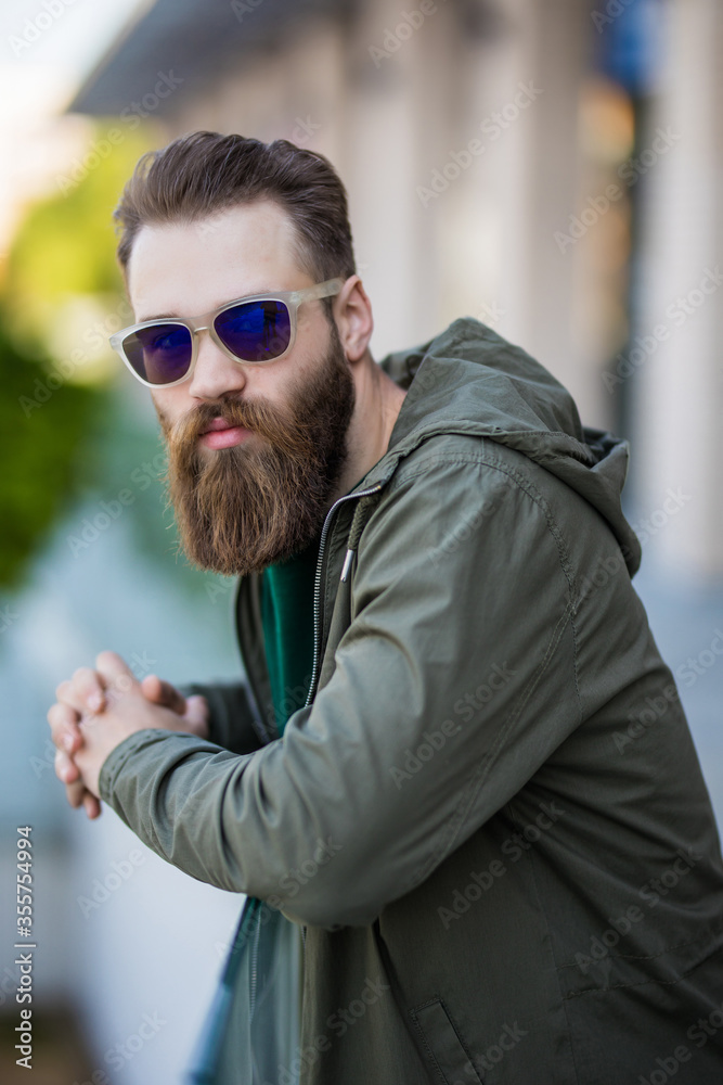Young bearded man with a beard and mustache with glasses posing on the street, outdoor portrait. Young bearded man with a beard and mustache with glasses posing on the street, outdoor portrait.