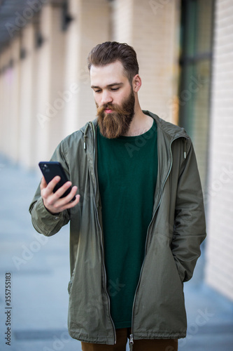 Bearded man reading a sms on his mobile phone in urban place on a sunny day